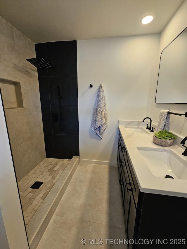 bathroom with a sink, baseboards, double vanity, and a tile shower