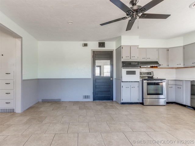 kitchen featuring oven, under cabinet range hood, a wainscoted wall, visible vents, and stainless steel electric stove