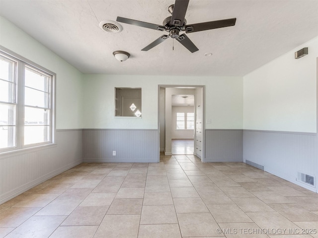 empty room with wainscoting, visible vents, and light tile patterned floors