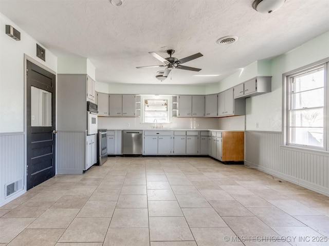 kitchen with visible vents, gray cabinetry, wainscoting, oven, and dishwasher