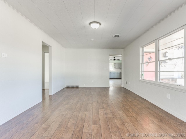 empty room with wood finished floors, visible vents, and baseboards