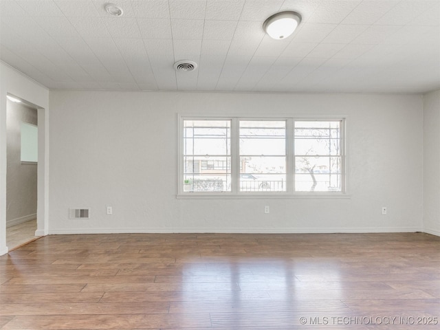 empty room with a wealth of natural light, wood finished floors, and visible vents