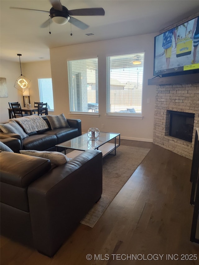 living area with baseboards, visible vents, a fireplace, ceiling fan, and dark wood-type flooring