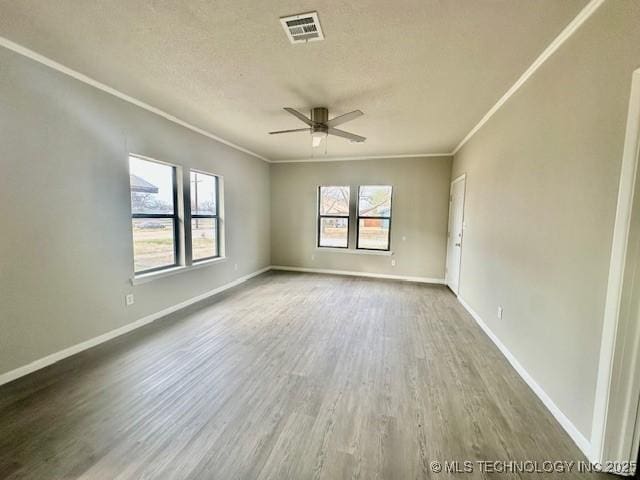 empty room with baseboards, visible vents, a ceiling fan, wood finished floors, and crown molding