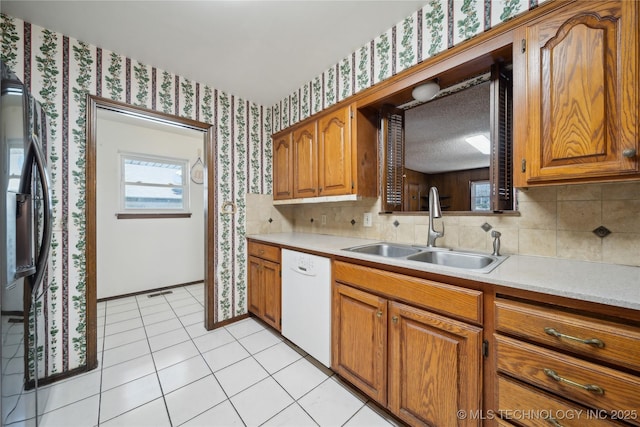 kitchen featuring light countertops, white dishwasher, a sink, and wallpapered walls