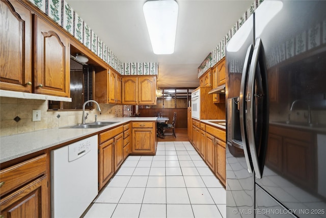 kitchen with light tile patterned floors, brown cabinetry, a sink, white appliances, and under cabinet range hood