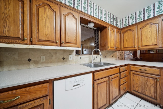 kitchen with brown cabinetry, light countertops, white dishwasher, and a sink