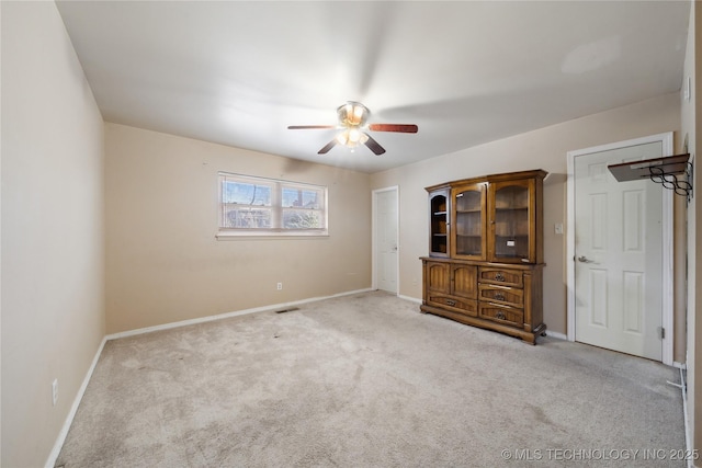 carpeted spare room with visible vents, baseboards, and a ceiling fan