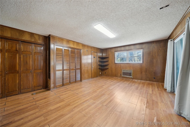 unfurnished bedroom featuring light wood-type flooring, wooden walls, a textured ceiling, and a wall mounted air conditioner