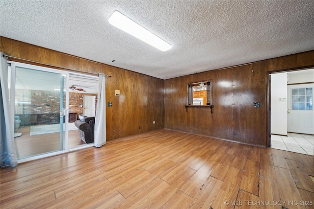 unfurnished room with light wood-style floors, a textured ceiling, and wood walls