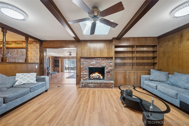 living area with wooden walls, a ceiling fan, beamed ceiling, wood finished floors, and a brick fireplace