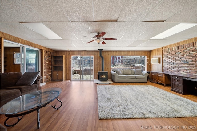 living area featuring a ceiling fan, a wood stove, wooden walls, and wood finished floors