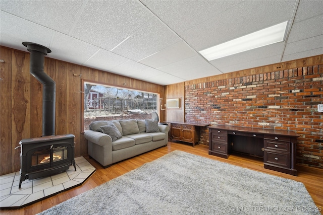 living area featuring light wood-type flooring, a wood stove, a drop ceiling, and wooden walls