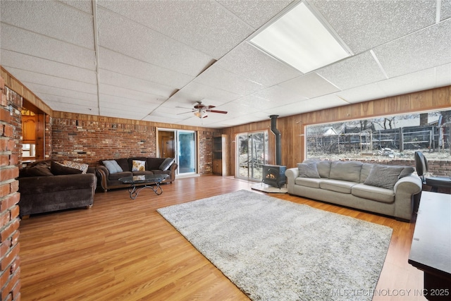 living room featuring a wood stove, a paneled ceiling, brick wall, and wood finished floors