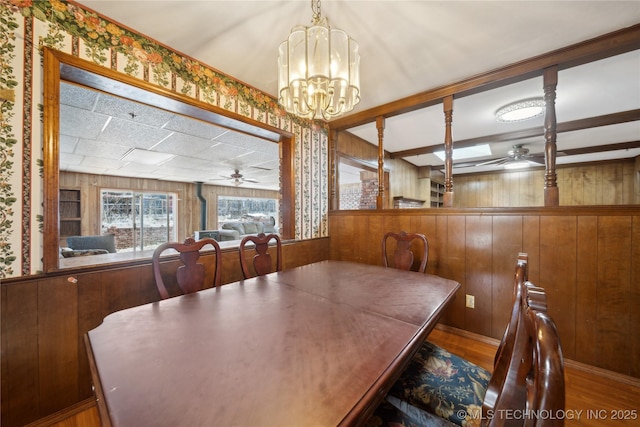 dining space featuring ceiling fan with notable chandelier, wood walls, wood finished floors, and beam ceiling