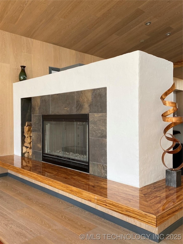 room details with wooden ceiling, a tiled fireplace, and wood finished floors