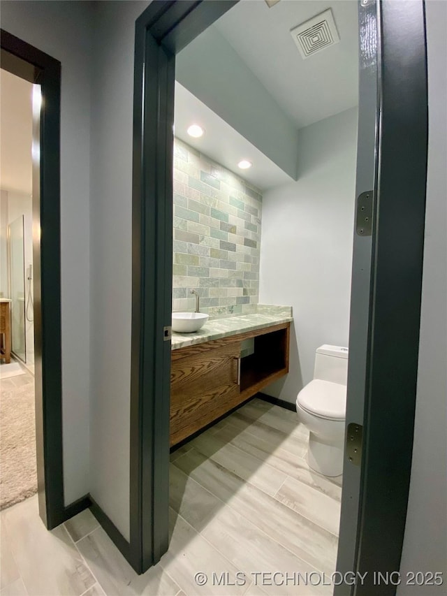 bathroom featuring baseboards, visible vents, toilet, vanity, and backsplash