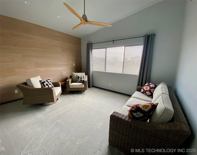 living area featuring carpet floors, ceiling fan, wooden walls, and vaulted ceiling