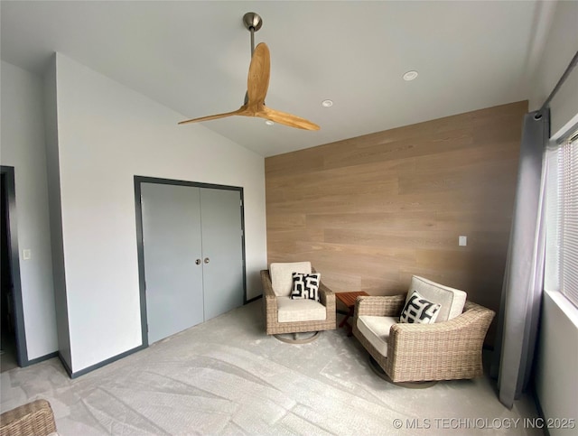 sitting room featuring vaulted ceiling, light colored carpet, and wood walls