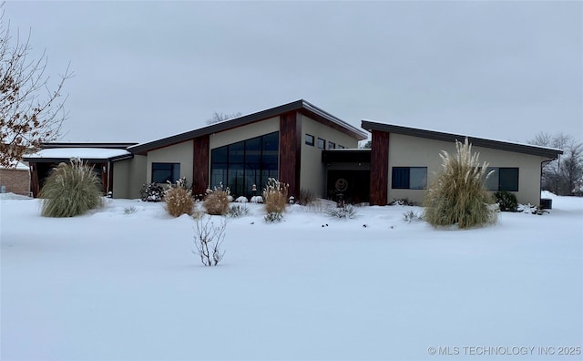 snow covered back of property featuring stucco siding