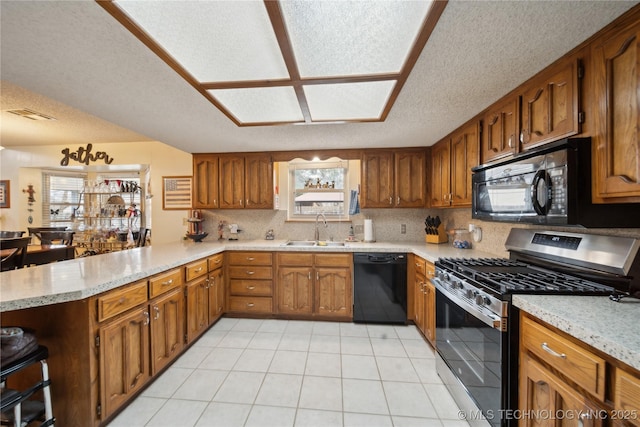 kitchen with a peninsula, a sink, black appliances, brown cabinets, and backsplash