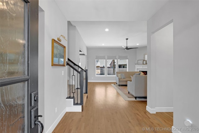 entrance foyer with a warm lit fireplace, baseboards, a ceiling fan, wood finished floors, and stairs