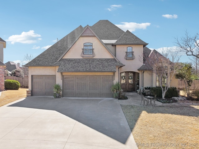 french country style house featuring french doors, stucco siding, a shingled roof, fence, and driveway