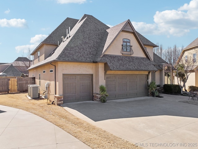 french country inspired facade featuring driveway, central AC unit, roof with shingles, and stucco siding