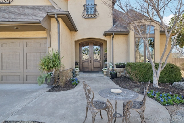 property entrance featuring a shingled roof, french doors, fence, and stucco siding