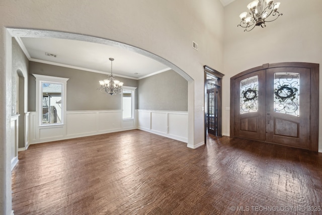 entrance foyer with a chandelier, arched walkways, french doors, and wood finished floors