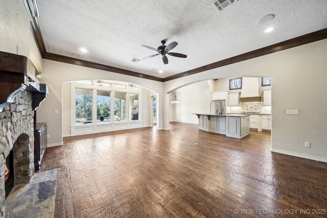 unfurnished living room with arched walkways, a stone fireplace, dark wood finished floors, and visible vents