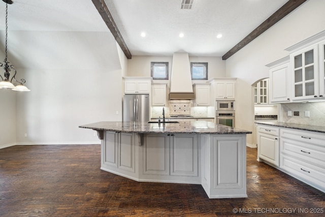 kitchen with a center island with sink, custom range hood, beam ceiling, stainless steel appliances, and a sink