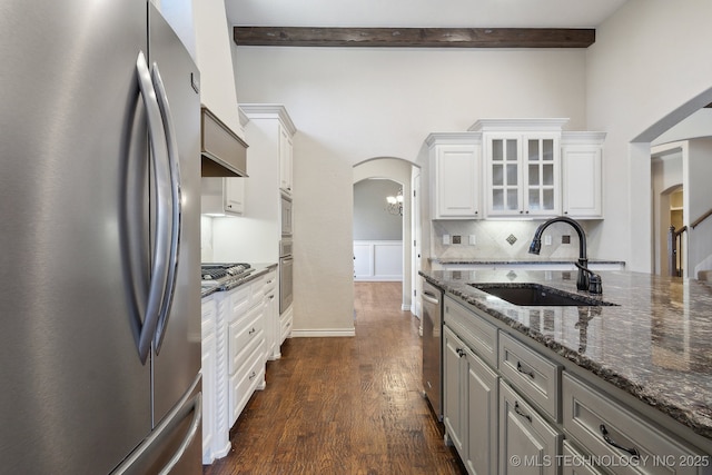 kitchen featuring arched walkways, appliances with stainless steel finishes, dark wood-type flooring, beamed ceiling, and a sink