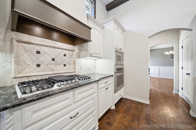 kitchen with arched walkways, dark wood finished floors, appliances with stainless steel finishes, white cabinetry, and premium range hood