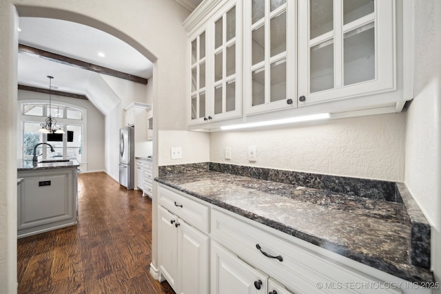 kitchen with dark wood-style floors, arched walkways, glass insert cabinets, freestanding refrigerator, and a sink