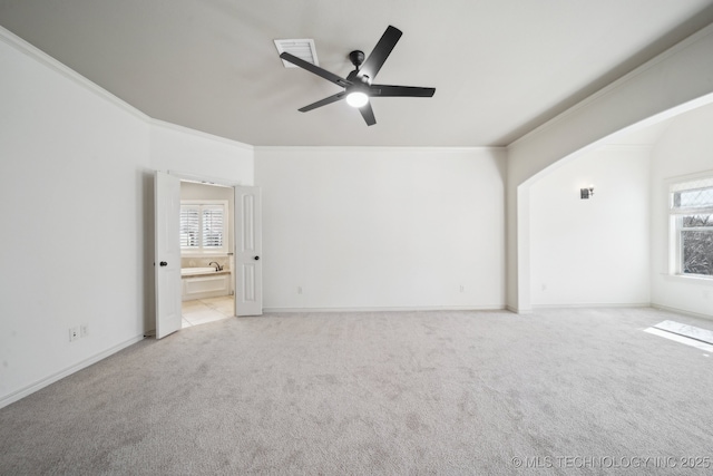 interior space with ceiling fan, light colored carpet, baseboards, ornamental molding, and ensuite bath