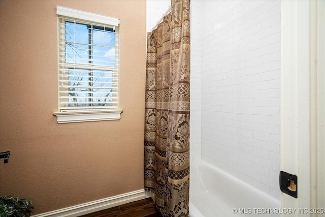 full bath with shower / bath combo, baseboards, wood finished floors, and a textured wall