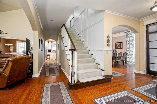 entrance foyer with arched walkways, crown molding, stairway, wood finished floors, and baseboards