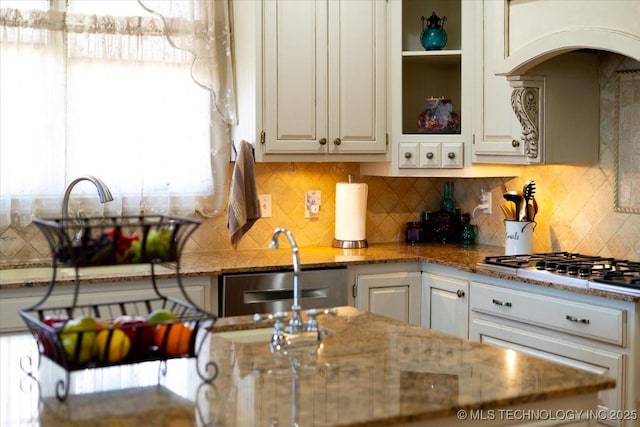 kitchen with tasteful backsplash, arched walkways, light stone countertops, stainless steel gas cooktop, and a sink