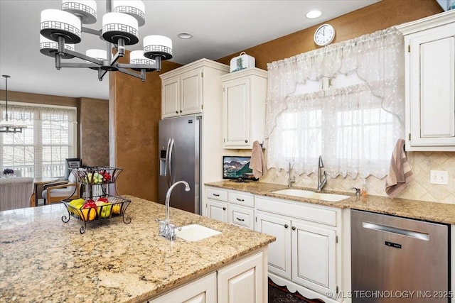 kitchen with appliances with stainless steel finishes, backsplash, a sink, and light stone countertops