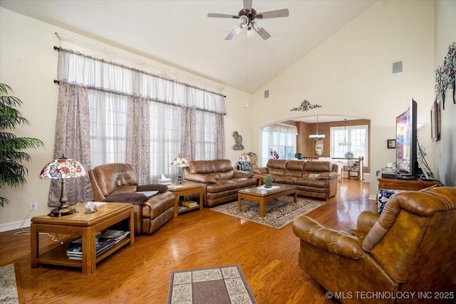 living room featuring visible vents, arched walkways, ceiling fan, light wood-type flooring, and high vaulted ceiling