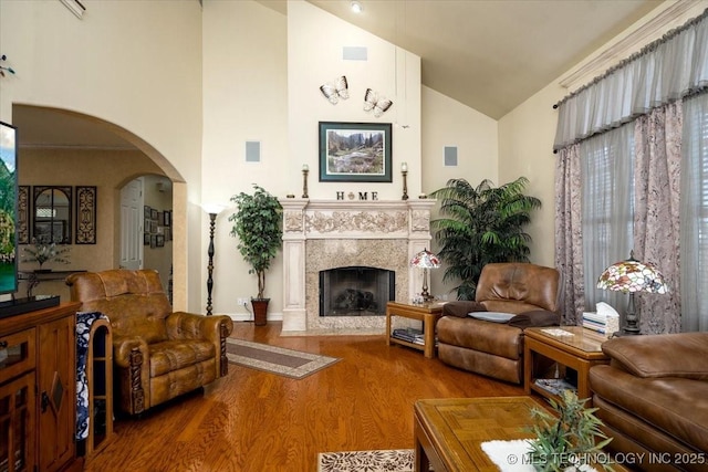 living area with a high end fireplace, arched walkways, high vaulted ceiling, and wood finished floors