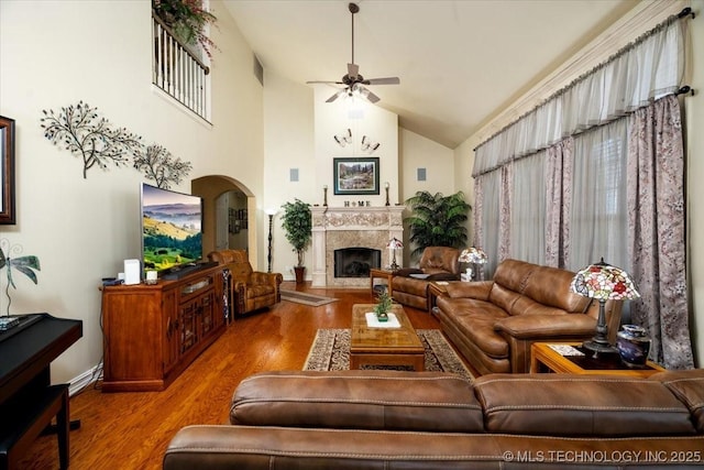 living area featuring arched walkways, a premium fireplace, ceiling fan, wood finished floors, and high vaulted ceiling