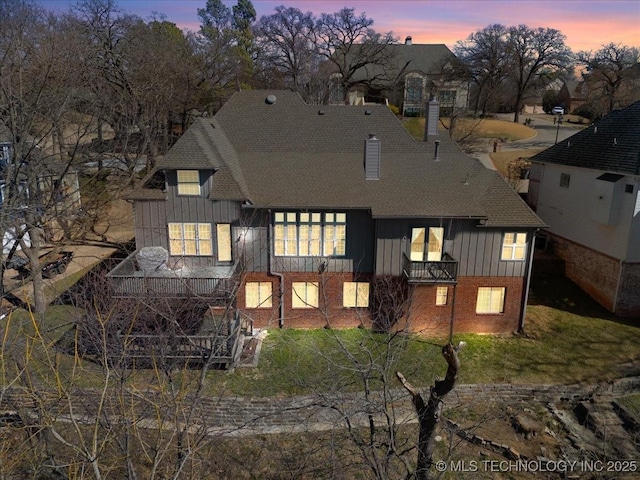 rear view of house with a shingled roof, a chimney, board and batten siding, and brick siding