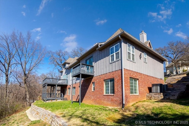 back of property with brick siding, a chimney, a lawn, central AC unit, and a balcony