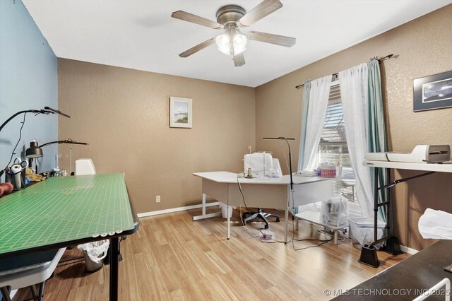 office space with a textured wall, light wood-style flooring, ceiling fan, and baseboards