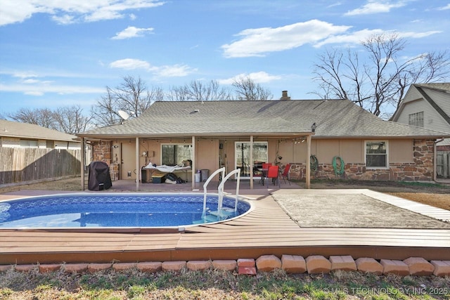 back of house with a fenced in pool, a deck, stone siding, and fence