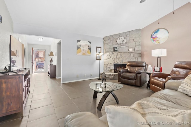 living area with baseboards, a stone fireplace, ceiling fan, tile patterned flooring, and lofted ceiling
