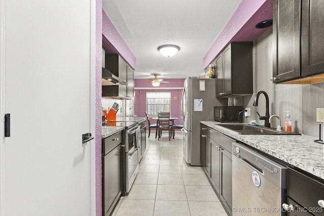 kitchen featuring light tile patterned floors, a ceiling fan, light stone countertops, appliances with stainless steel finishes, and a sink
