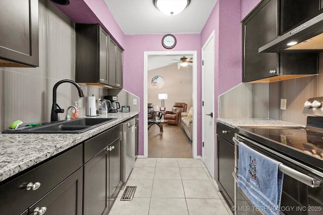 kitchen featuring a ceiling fan, light tile patterned flooring, wall chimney exhaust hood, stainless steel appliances, and a sink